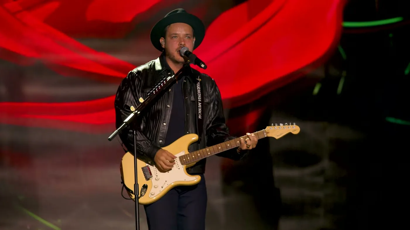 Israel canta e toca guitarra diante de um cenário vermelho no vídeo de Conto de Fadas