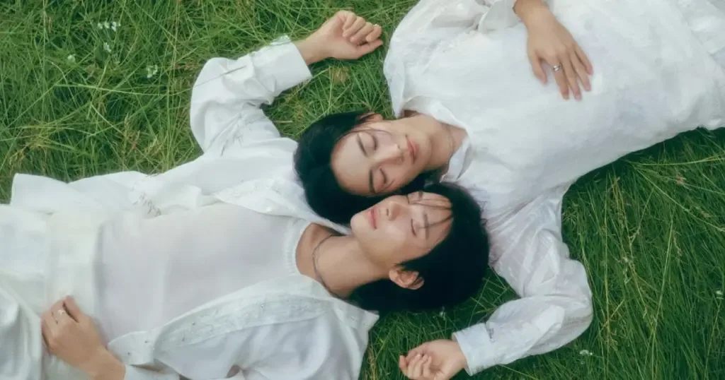 Jeonghan e Joshua aparecem deitados na grama, com roupas claras, em imagem promocional de DREAMSCAPE.