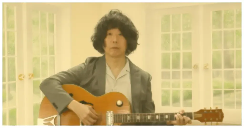 Shintaro Sakamoto toca guitarra diante de um fundo claro esverdeado.
