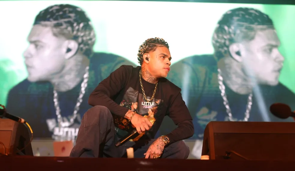 MC Cabelinho sentado no palco diante de um telão com seu rosto.