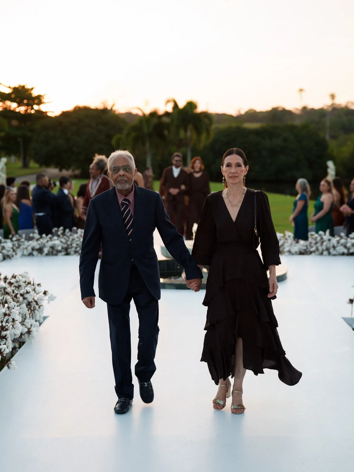 Gilberto Gil e Flora Gil caminham de mãos dadas entre convidados